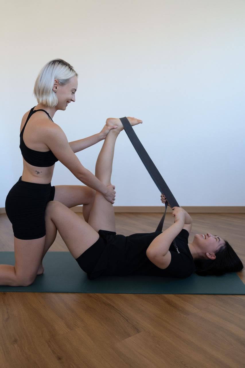 Instructor helping a client stretch her leg with a strap during a private stretching session