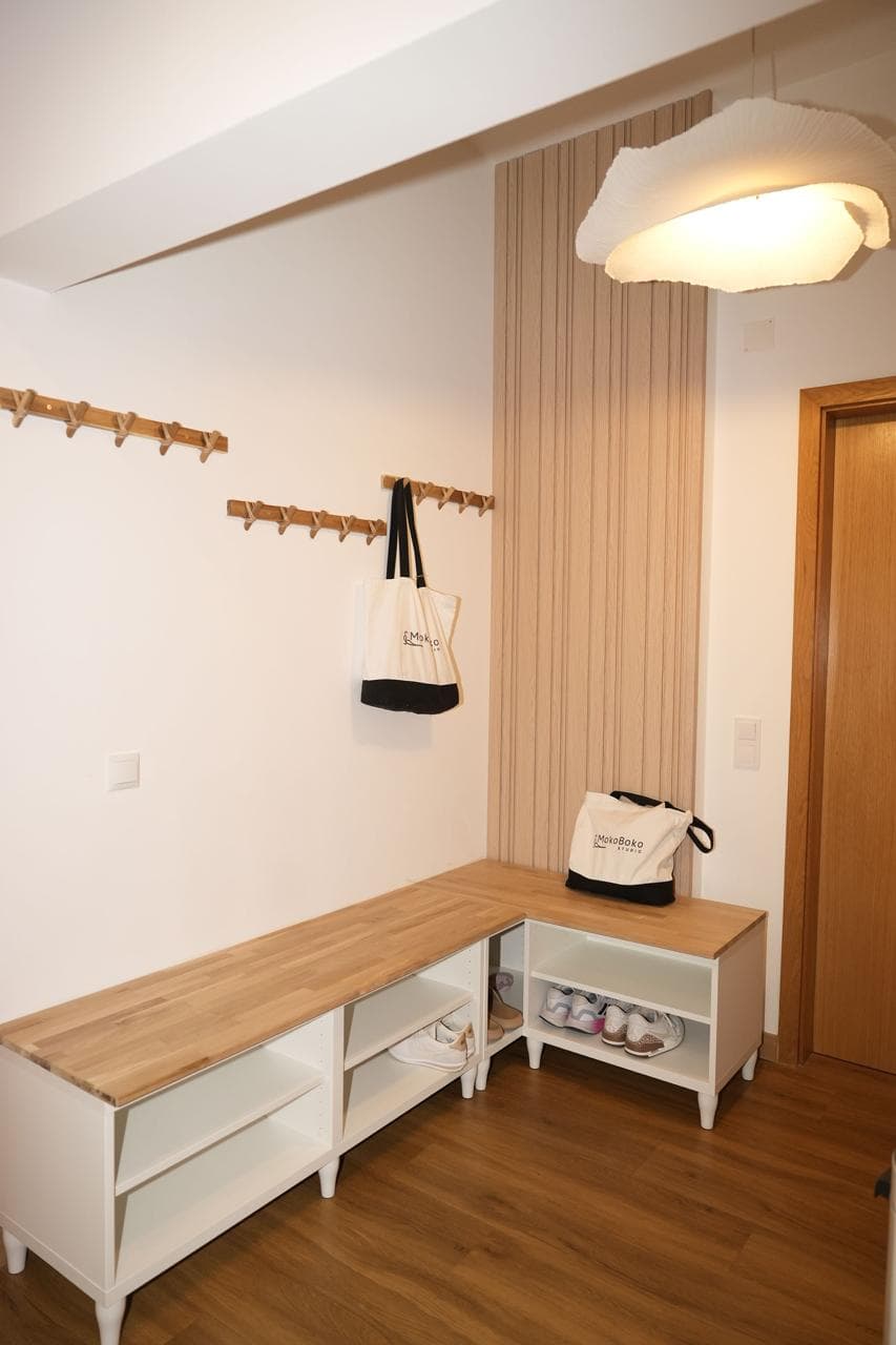 The studio entryway featuring wall-mounted wooden coat racks, a bench with shoe storage cubbies, and canvas tote bags printed with the "MokoBoko Studio" logo.