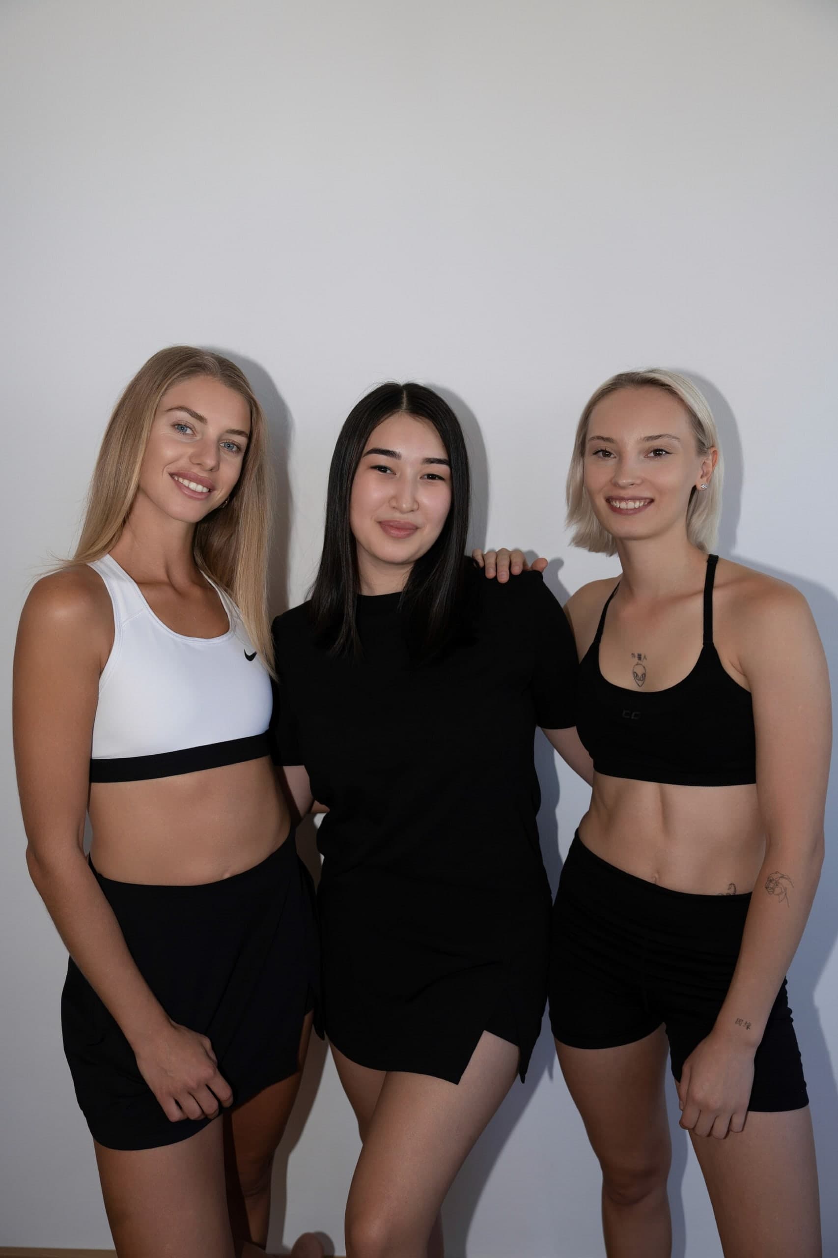 Three smiling women in black and white workout wear standing together at MokoBoko