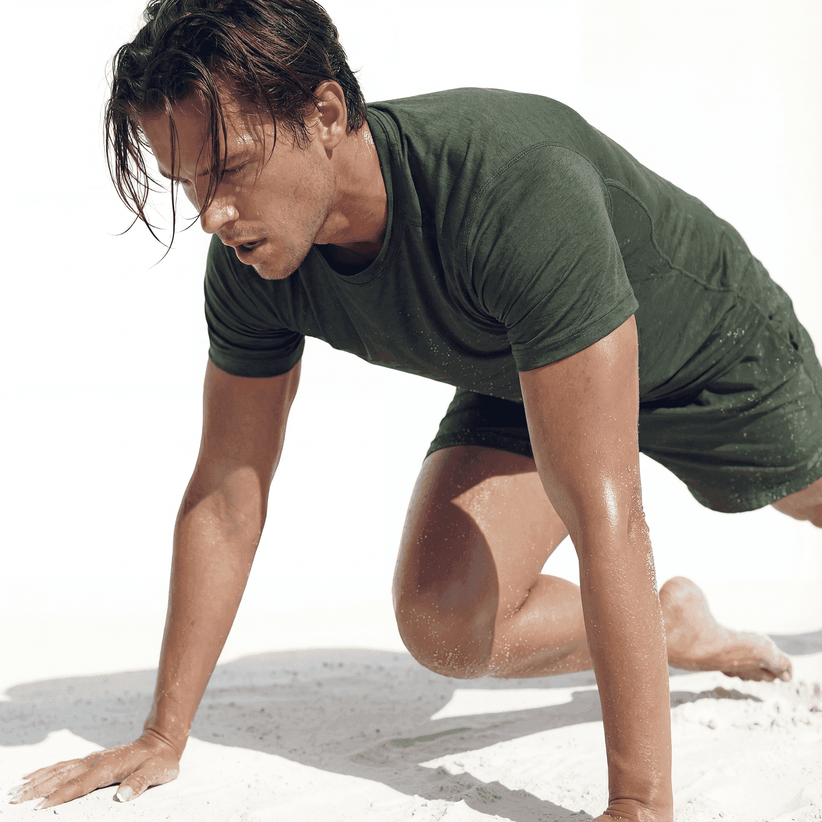 Man in a green T-shirt doing a bear crawl on white sand